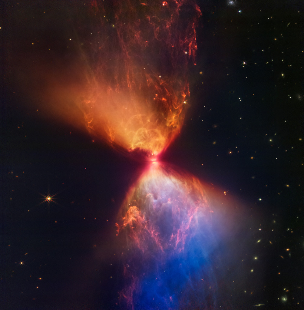 The Protostar within L1527. It looks like a hourglass shaped cluster of red, orange, blue, and yellow matter.
